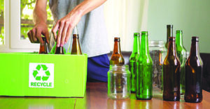 Person placing glass bottles into a household recycling bin.