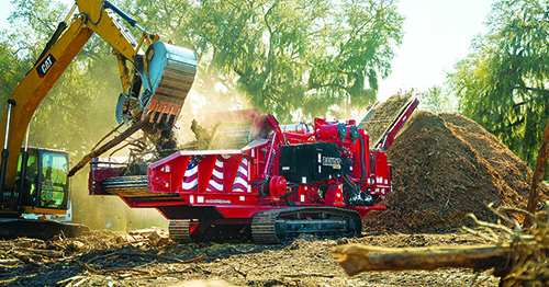 Tracked wood grinder processing material with excavator