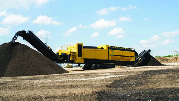 Tracked industrial screening machine processing material into stockpiles at an outdoor recycling operation