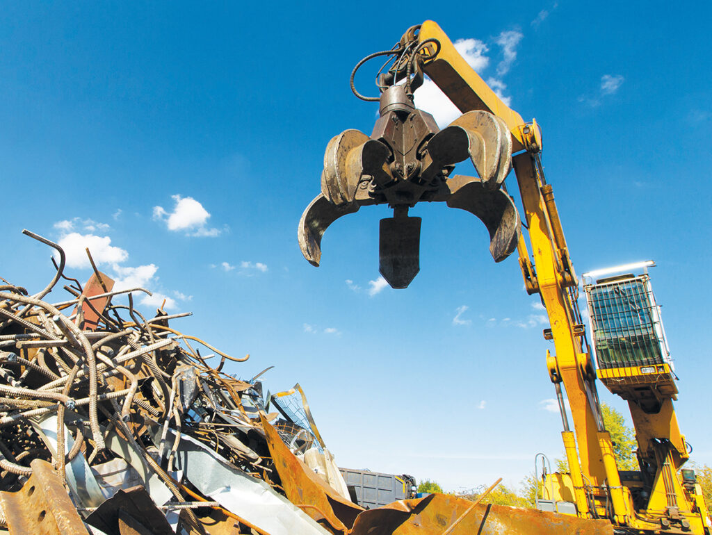 Material handler with an orange peel grapple loading scrap metal at a recycling yard.