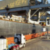 Steel coils being loaded onto a cargo ship at a port for international steel imports.