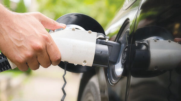 Mans hand inserting charger plug into electric car in green environment background. New energy vehicle, NEV is being loaded with electricity power. Ecology, modern day cars Electric vehicle connected to a DC fast charging station.
