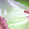 Hands stretching a sheet of plastic film representing post consumer plastic recycling.