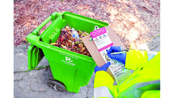 Worker inspecting a Recology compost cart as part of the company's sustainability and recycling operations.
