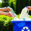People placing plastic bottles into a blue recycling bin for collection and recycling