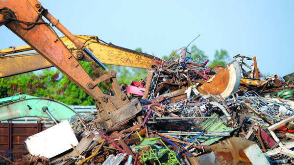 Excavator magnet lifting steel scraps from recycling materials pile at scrap yard in recycling factory. Excavator with electro and magnetic sucker magnet chuck. Special excavator. Scrap metal magnet. Scrap metal recycling yard illustrating metal market volatility