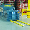BaleTech Pathfinder industrial baler with blue steel housing and yellow loading rails inside a warehouse.