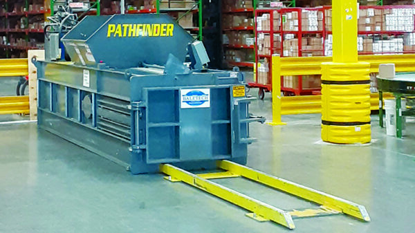 BaleTech Pathfinder industrial baler with blue steel housing and yellow loading rails inside a warehouse.