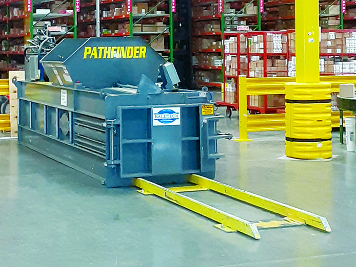 BaleTech Pathfinder industrial baler with blue housing and yellow loading rails inside a warehouse.