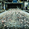 Shredded battery materials and black mass moving along a conveyor belt inside a battery recycling facility.