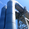 Industrial steel processing equipment with large metal structures and piping against a clear blue sky. Featured Image Description