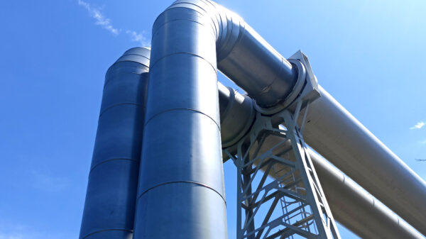 Industrial steel processing equipment with large metal structures and piping against a clear blue sky. Featured Image Description